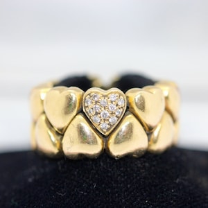 May include: A gold ring with a heart-shaped design. The heart is set with small diamonds. The ring is made of multiple hearts that are linked together.