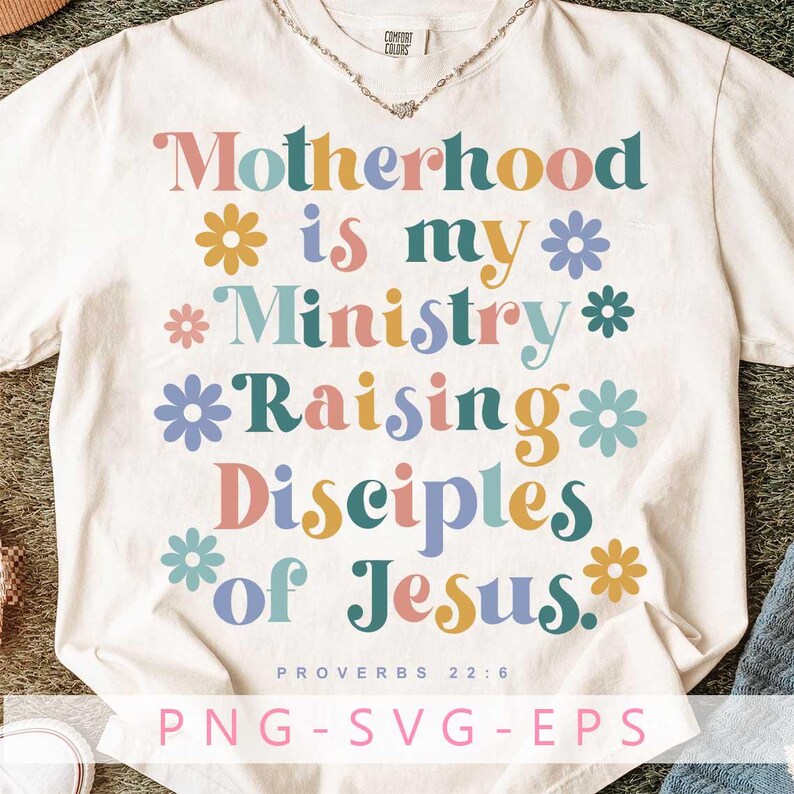 May include: Cream-colored t-shirt with the text "Motherhood is my Ministry Raising Disciples of Jesus" in colorful, floral-decorated letters. The shirt also features the text "PROVERBS 22:6" and "PNG-SVG-EPS".