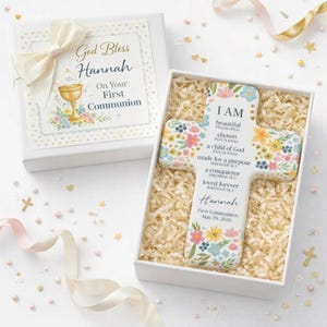 May include: A white gift box with a cream bow and a decorative cross. The cross is floral-themed with the words "I AM beautiful, chosen, a child of God, made for a purpose, a conqueror, loved forever." The box reads "God Bless Hannah On Your First Communion."