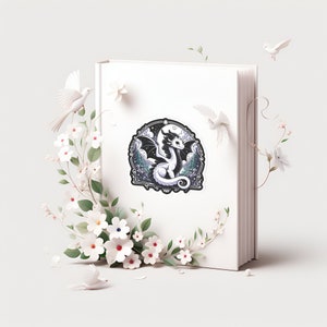K&ouml;nnte beinhalten: Ein wei&szlig;es Buch mit einem schwarz-wei&szlig;en Aufkleber eines Drachen in einer Waldszene. Der Aufkleber ist von wei&szlig;en Blumen umgeben.