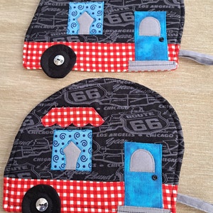 May include: Two black and white pot holders shaped like vintage campers with red and white checkered roofs. The pot holders have a Route 66 theme with the text "Route 66" and "Los Angeles" printed on them.