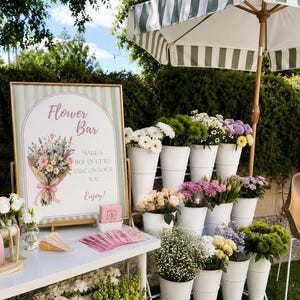 May include: A flower bar setup featuring a rectangular sign with green stripes, the text Flower Bar, and a bouquet illustration. Beside it, a white table holds pink napkins and wooden sticks. White buckets display various fresh flowers.