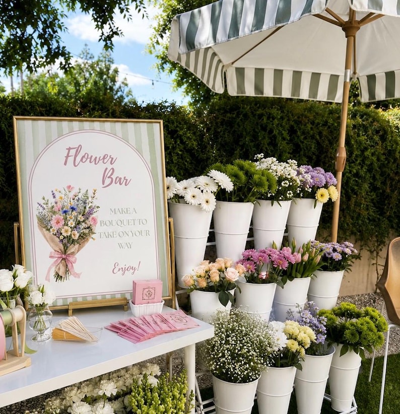 May include: A flower bar setup featuring a rectangular sign with green stripes, the text Flower Bar, and a bouquet illustration. Beside it, a white table holds pink napkins and wooden sticks. White buckets display various fresh flowers.