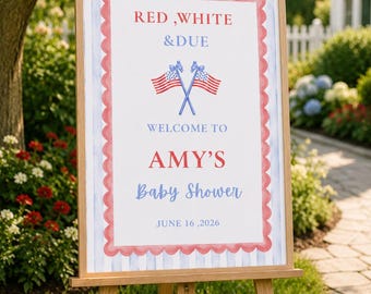 May include: Wooden easel displaying a sign with patriotic colors and text. The sign reads "RED, WHITE & DUE" and "WELCOME TO AMY'S Baby Shower JUNE 16, 2026". Decorative flags are crossed below the title.