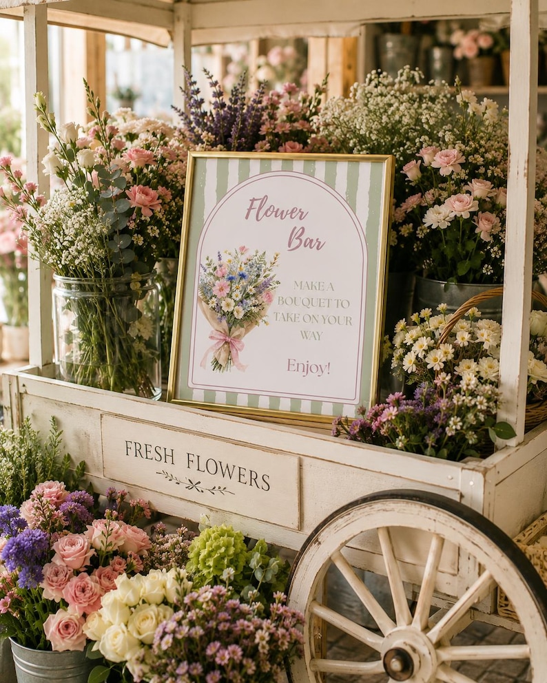 May include: A gold-framed sign with a green and white striped background features an illustration of a floral bouquet and the text Flower Bar, MAKE A BOUQUET TO TAKE ON YOUR WAY, and Enjoy! The sign sits on a white wooden cart with wheels.