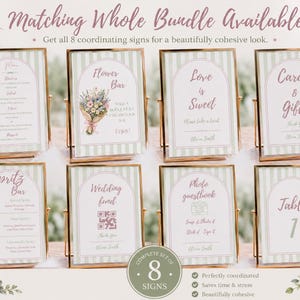 May include: A set of eight rectangular event signs in gold metal frames, featuring a sage green striped background and arched white panels with pink text. The signs include labels for Menu, Flower Bar, Love is Sweet, Cards & Gifts, Spritz Bar, Wedding Fund, Photo guestbook, and Table 1.