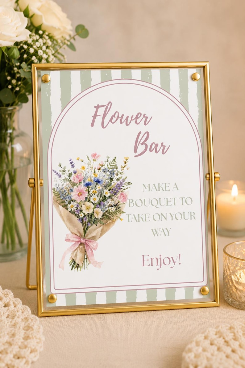 May include: A rectangular sign in a gold metal frame featuring a green and white striped background. The sign displays the text "Flower Bar," "MAKE A BOUQUET TO TAKE ON YOUR WAY," and "Enjoy!" alongside a colourful illustration of a flower bouquet.