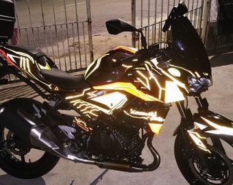 Może przedstawiać: Czarny motocykl z żółtymi i pomarańczowymi odblaskowymi akcentami. Motocykl ma szybę i kufer górny.