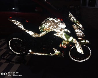 Może przedstawiać: Czarny motocykl z odblaskowym wzorem graficznym Venom. Motocykl ma biało-czarne malowanie z czerwonymi akcentami. Motocykl stoi na stojaku, a koła są widoczne.