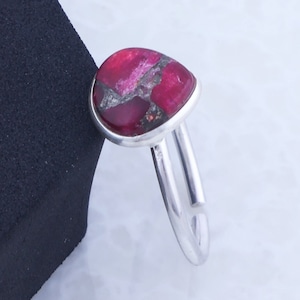 Op de afbeelding: Een zilveren ring met een roze en grijze edelsteen. De ring ligt op een wit oppervlak.