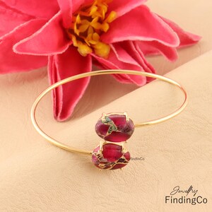 May include: Gold bangle bracelet with two red and green gemstone accents. Jewellery FindingCo.