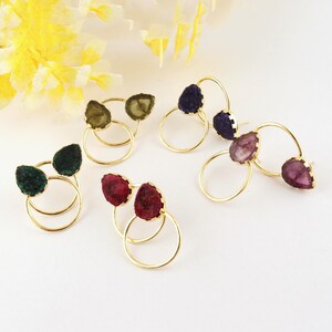 May include: Four pairs of stud earrings featuring gold-tone circular frames paired with irregular, rough-cut gemstone accents in shades of dark green, olive, deep purple, and magenta. Each earring set consists of a metal ring and a stone piece.