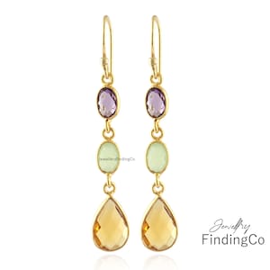 May include: Gold earrings with three gemstone drops. The top drop is a purple amethyst, the middle drop is a light green stone, and the bottom drop is a teardrop-shaped amber stone.