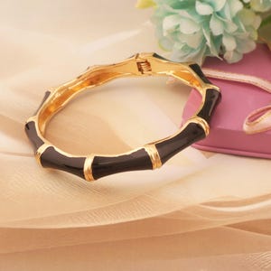 May include: A gold-tone hinged bangle bracelet with a bamboo design. The bracelet features black enamel segments with gold accents. The bracelet is a stylish accessory.