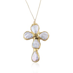 May include: A gold-toned necklace featuring a cross-shaped pendant composed of five irregular, iridescent white baroque pearls. Each pearl is individually encased in a textured, organic-looking gold metal frame, suspended from a delicate gold chain.