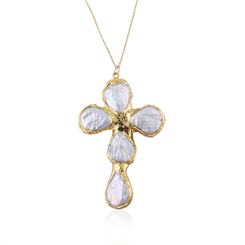 May include: A gold-toned necklace featuring a cross-shaped pendant composed of five irregular, iridescent white baroque pearls. Each pearl is individually encased in a textured, organic-looking gold metal frame, suspended from a delicate gold chain.