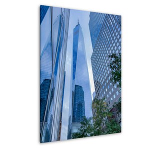 Puede incluir: Una vista de ángulo bajo de un rascacielos moderno y alto con una cima puntiaguda, rodeado de otros edificios. El edificio está hecho de vidrio y refleja el cielo y otros edificios. El cielo es azul y los edificios son principalmente grises.