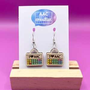 May include: A pair of wooden earrings featuring a colourful keyboard design and the text "I ❤️ AAC". The earrings hang from silver hooks and are displayed on a white card with the "AAC creative" logo.