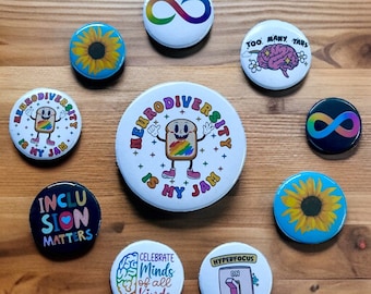Insignias con temática de neurodiversidad e inclusión en diferentes tamaños y opciones de reverso de metal o plástico.
