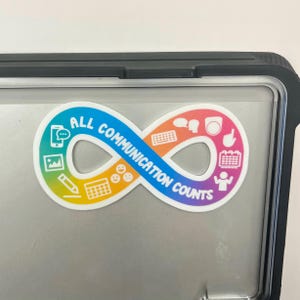 May include: A rainbow-colored infinity symbol sticker with the text "ALL COMMUNICATION COUNTS" and various communication icons. The sticker is on a silver laptop.