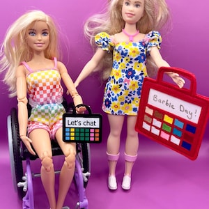 May include: Two Barbie dolls, one in a wheelchair, holding colorful felt boards with the text "Let's chat" and "Barbie Day!"