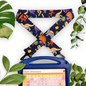 May include: A blue tablet case with a dinosaur-themed strap. The strap has colourful dinosaurs, pencils, and other school graphics on a navy blue background. The tablet screen displays the text "I love dinosaurs".