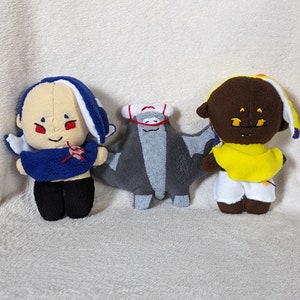 May include: Three handmade plush dolls. One doll has a tan face, blue and white hair, a blue top, and black pants. The second doll is a gray bat-like creature. The third doll has a brown face, yellow top, and white shorts.