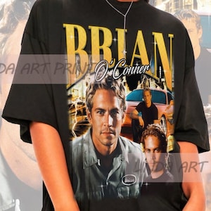 May include: Black oversized t-shirt with a graphic print of Paul Walker as Brian O'Conner from the Fast and Furious franchise. The print features a collage of images of Walker in the movie, including a car and a cityscape.