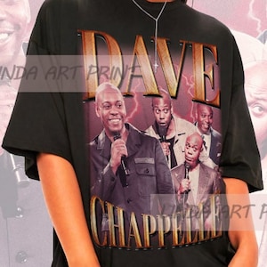 May include: Black oversized t-shirt with a graphic print of Dave Chappelle and the text "Dave Chappelle" in gold lettering.