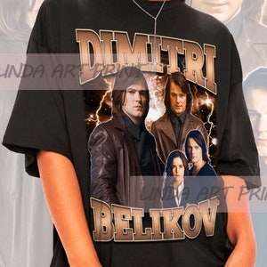 Puede incluir: Camiseta negra de gran tamaño con un estampado gráfico de una banda llamada "DIMITRI BELIKOV". Los miembros de la banda aparecen en un estilo vintage con rayos y un fondo estrellado.