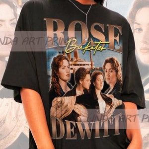 Może przedstawiać: Czarny, oversize'owy T-shirt z nadrukiem graficznym Rose DeWitt Bukater z filmu Titanic. Grafika przedstawia Rose i Jacka na statku z tekstem "Rose DeWitt" i "Bukater" złotymi literami.