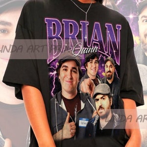 以下が含まれることがあります： 黒色のオーバーサイズTシャツに、4人の男性の顔のグラフィックプリントが施されています。シャツには「BRIAN Quinn」という文字が紫でプリントされています。シャツは、長い黒髪とサングラスをかけた人が着用しています。