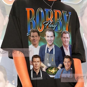 May include: Black t-shirt with a graphic print of Bobby Flay and other chefs. The graphic is in a retro style with a lightning bolt design. The t-shirt is oversized and has a crew neck.