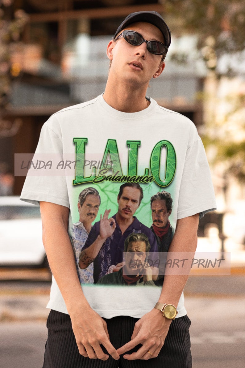 May include: White t-shirt with a green and white graphic print of the text "Lalo Salamanca" and four men's faces.