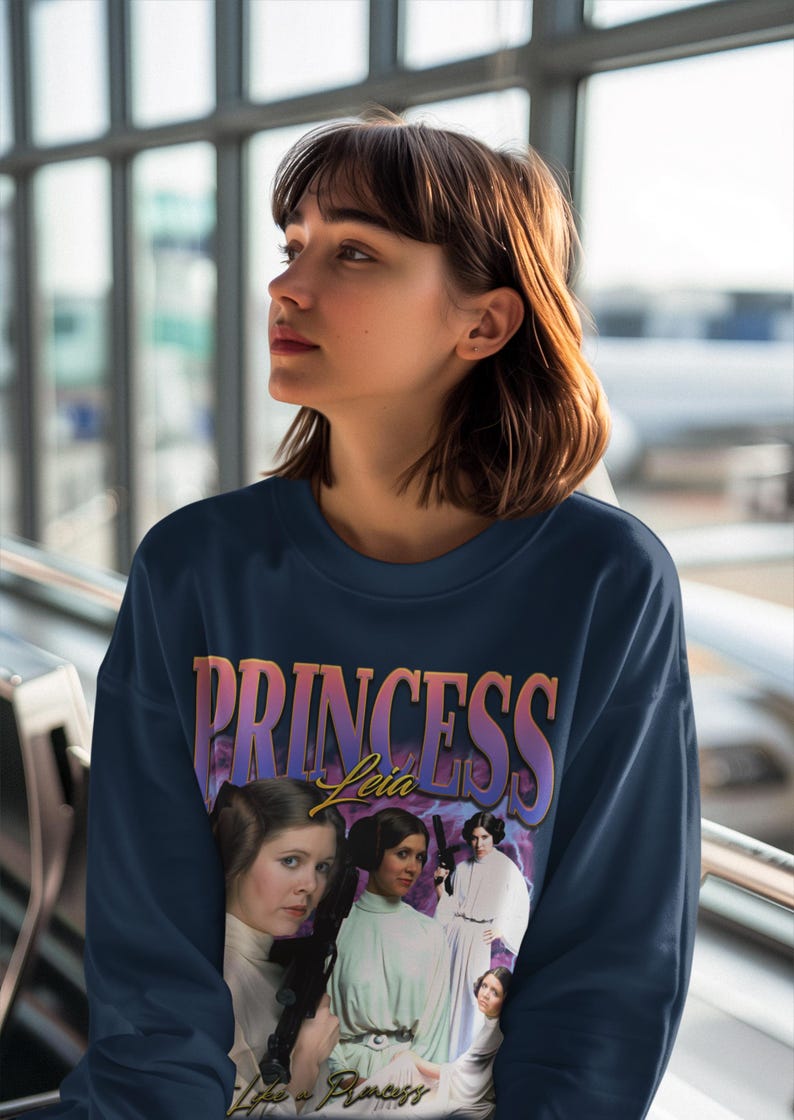 May include: A navy blue sweatshirt with a vintage-style graphic print of Princess Leia from Star Wars. The graphic features a collage of images of Princess Leia in different poses, with the text "Princess Leia" in a colorful, gradient font.