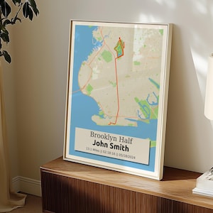 May include: Framed map print of the Brooklyn Half marathon route, with a red line marking the course. The print includes the text "Brooklyn Half John Smith 13.1 Miles || 02:18:16 || 05/18/2024" on a light blue background. The frame is white.