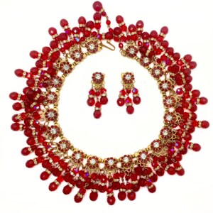 May include: A red and gold beaded necklace and earrings set. The necklace features a cascading design with red beads and gold accents. The earrings are dangle style with red beads and gold accents.