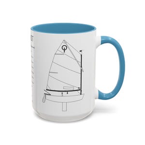Op de afbeelding: Witte keramische mok met een blauwe binnenkant en handvat. De mok heeft een zwarte lijntekening van een zeilboot met het woord "SAILOR" en andere tekst op de zijkant. De mok heeft een standaardformaat voor koffie of thee.