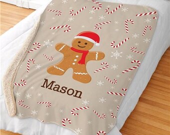 May include: A beige fleece blanket with a gingerbread man wearing a red hat and scarf. The blanket is decorated with red and white candy canes and snowflakes. The text "Mason" is printed on the blanket.