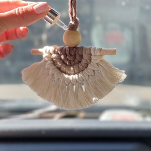 May include: A beige and brown macrame car air freshener with a wooden bead and a glass bottle with a dropper.