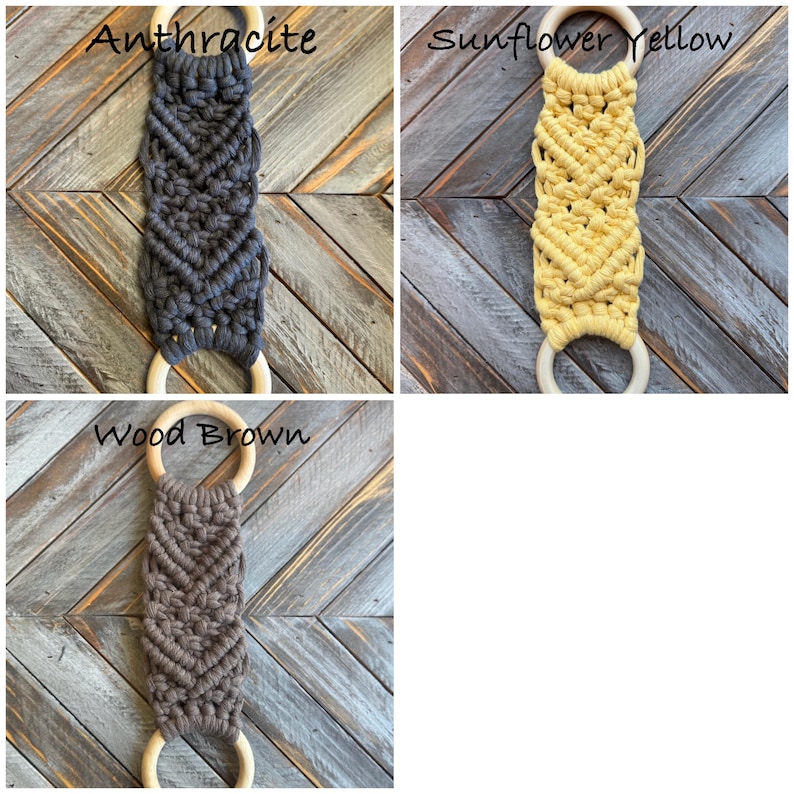 Pu&ograve; includere: Tre arazzi in macram&egrave; con corda annodata in antracite, giallo girasole e marrone legno. Ogni pezzo presenta un motivo a chevron ed &egrave; fissato a due anelli di legno liscio di colore chiaro alle estremit&agrave; superiore e inferiore.