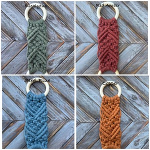 Pu&ograve; includere: Quattro portasciugamani in macram&egrave; con un motivo a nodi a chevron fissati ad anelli in legno chiaro. I colori sono etichettati come Eucalyptus, Red Amber, Steel Blue e Copper. Ogni pezzo mostra un colore di corda tessile distinto.