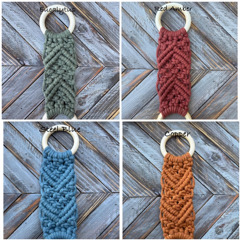 Pu&ograve; includere: Quattro portasciugamani in macram&egrave; con un motivo a nodi a chevron fissati ad anelli in legno chiaro. I colori sono etichettati come Eucalyptus, Red Amber, Steel Blue e Copper. Ogni pezzo mostra un colore di corda tessile distinto.