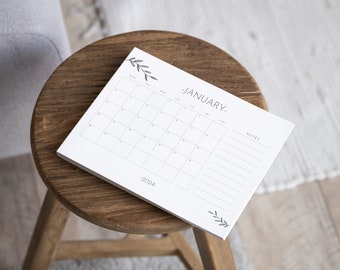 May include: A white calendar with a simple design featuring a floral motif. The calendar is for January 2024 and has a notes section.
