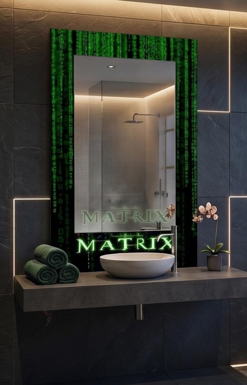 K&ouml;nnte beinhalten: Ein rechteckiger Wandspiegel mit einem schwarzen Rahmen, der mit gr&uuml;nen digitalen Codemustern und dem Wort MATRIX in leuchtend gr&uuml;nen Buchstaben verziert ist. Der Spiegel reflektiert ein Badezimmer mit einem wei&szlig;en Waschbecken.