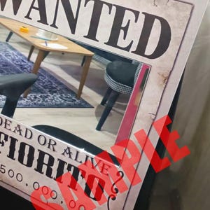K&ouml;nnte beinhalten: Ein rechteckiges Poster mit einem Steckbrief im Vintage-Stil mit dem Text WANTED, DEAD OR ALIVE, FIORITO und 500.000.000. Das Design hat ein gealtertes Papier-Aussehen mit einem gro&szlig;en, roten, durchscheinenden SAMPLE-Wasserzeichen in der Mitte.
