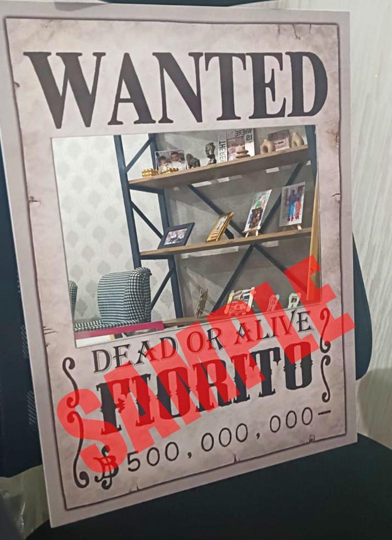 K&ouml;nnte beinhalten: Ein rechteckiges Poster mit beigem, verwittertem Hintergrund und dem Wort WANTED in gro&szlig;en schwarzen Buchstaben oben. Unter einem zentralen rechteckigen Ausschnitt steht der Text DEAD OR ALIVE, FIORITO und 500.000.000 mit rotem Stempel.