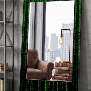 May include: A rectangular floor mirror featuring a black frame decorated with green digital code patterns and the word MATRIX in glowing green letters at the bottom. The reflective surface shows a brown leather armchair, a stack of books, and a lamp.