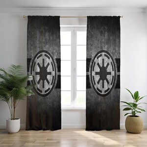 May include: A pair of floor-length curtains featuring a dark gray and black distressed texture. Each panel displays a large, centered circular emblem with a stylized eight-spoked star design in black, set against a horizontal black band.