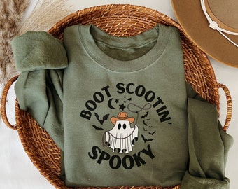 May include: A green sweatshirt featuring a ghost wearing a cowboy hat and lasso. The text "Boot Scootin' Spooky" is printed on the front of the sweatshirt.
